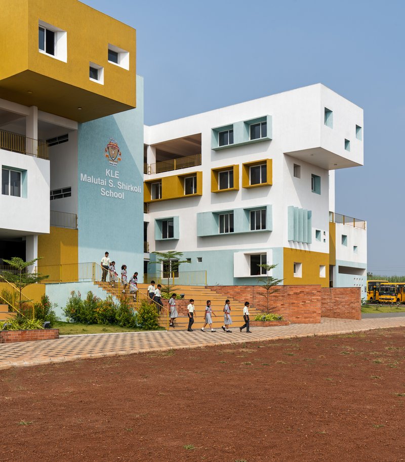 Street view of the stacked white and yellow volumes with students walking on the brick-paved courtyard