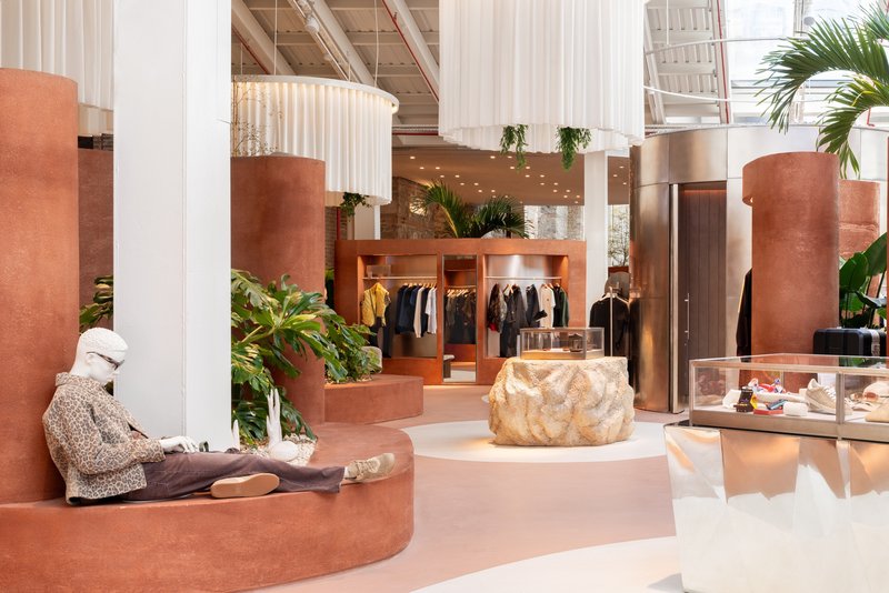 Retail interior with terracotta curved seating elements and tropical plants beneath sheer white drapery