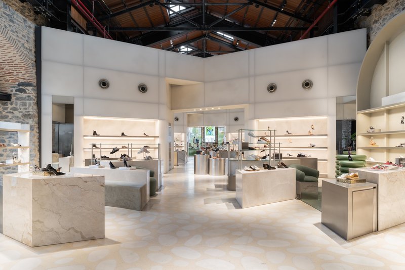Retail floor with white display volumes and lit shelving beneath exposed timber ceiling and industrial steel trusses