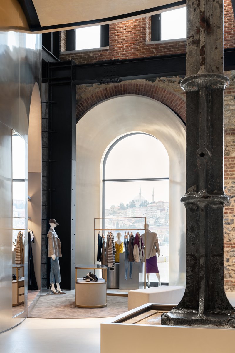 Retail interior with exposed brick arch, weathered column, and arched window framing a distant hillside view