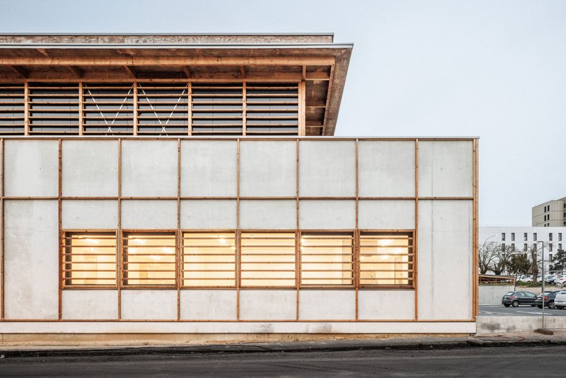 Street elevation showing the translucent panel and timber grid facade illuminated from within at twilight