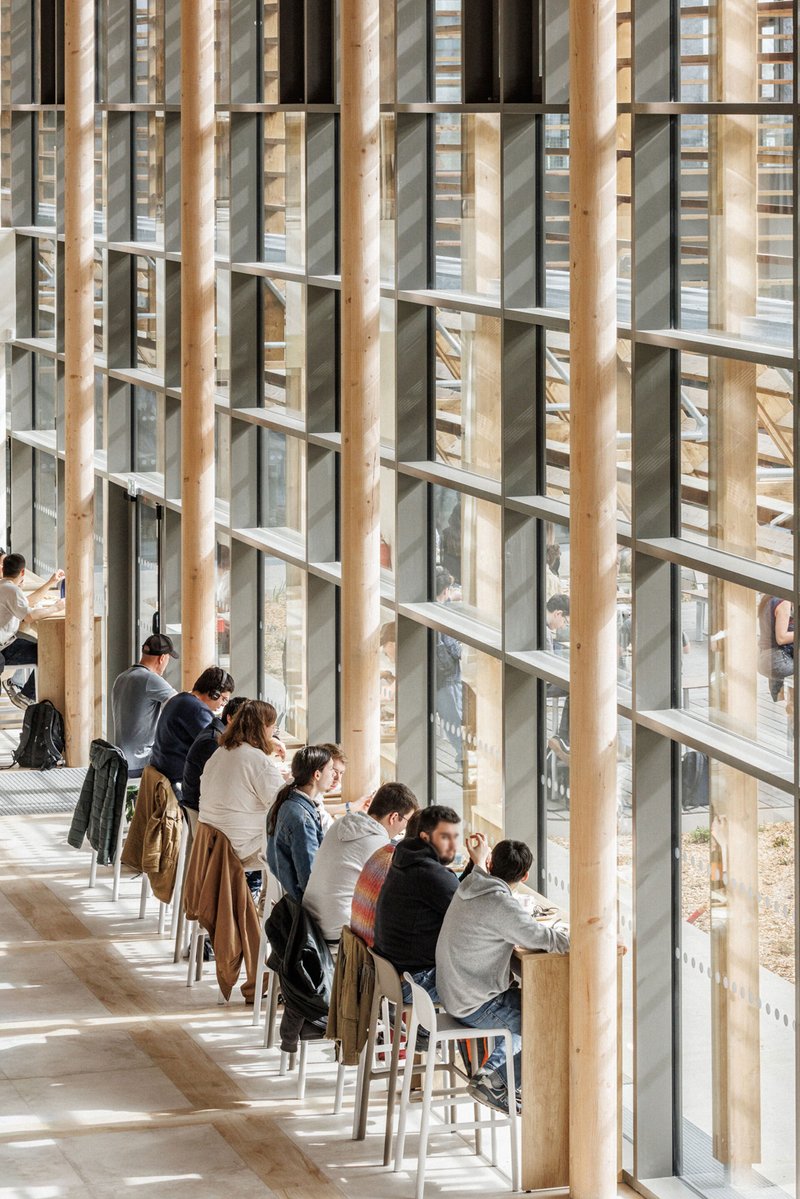 Window counter lined with visitors seated on stools between vertical timber mullions and glass panels