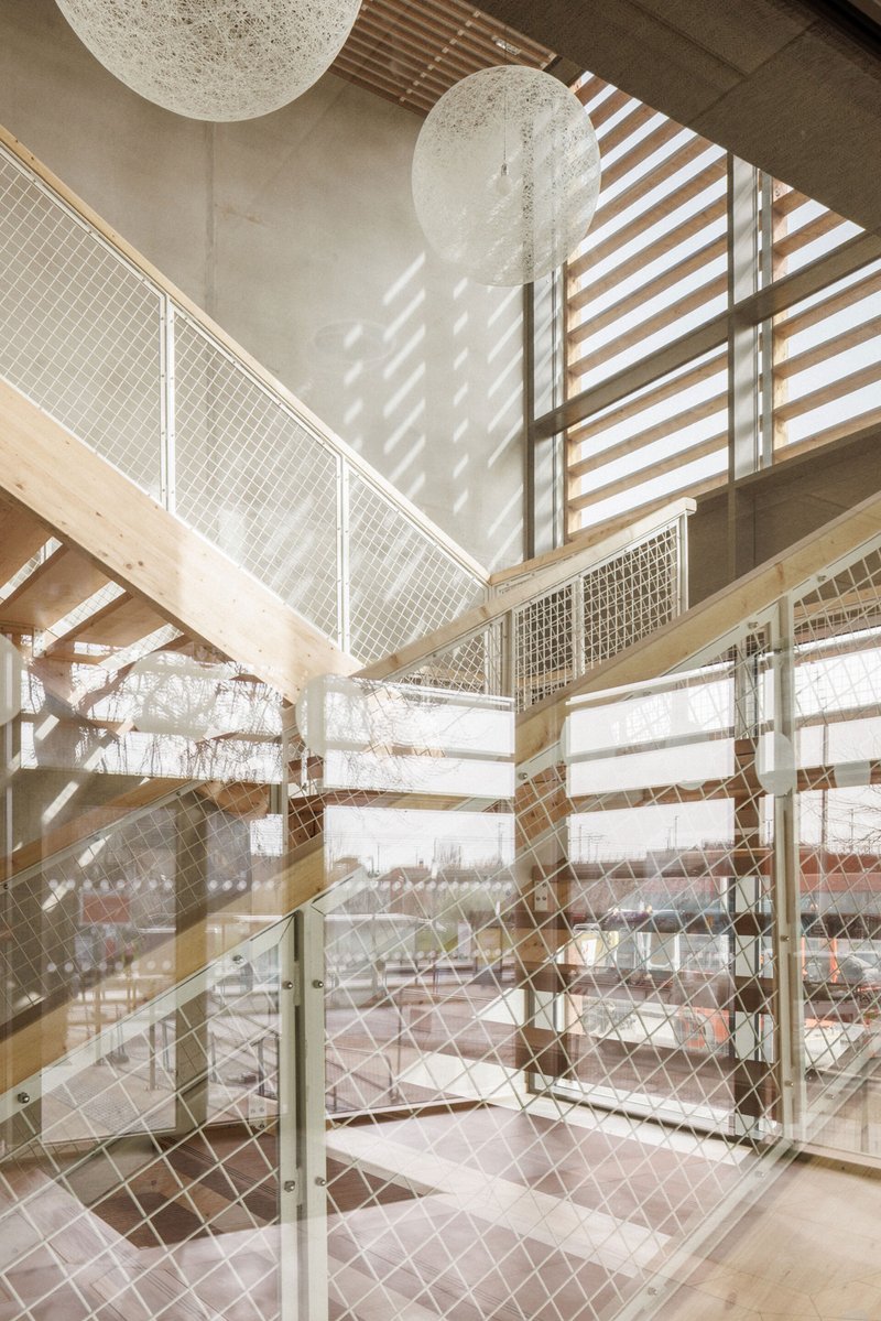 Stairwell with wire mesh balustrades and timber louvers casting diagonal shadow patterns across white walls