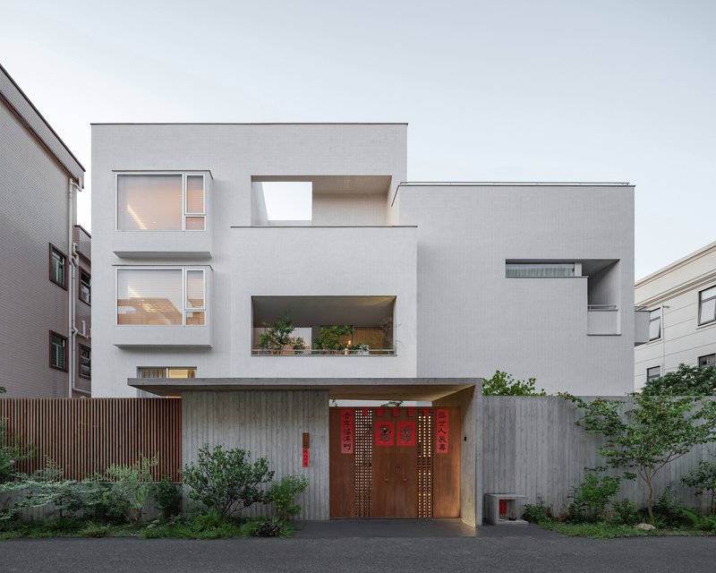 Street view showing the layered white volumes with recessed balconies and timber entry gate