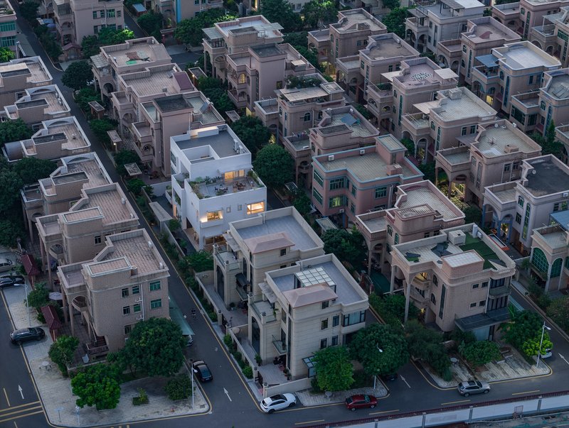 Drone view of residential blocks at dusk showing a white multi-level house among pink-toned neighbors