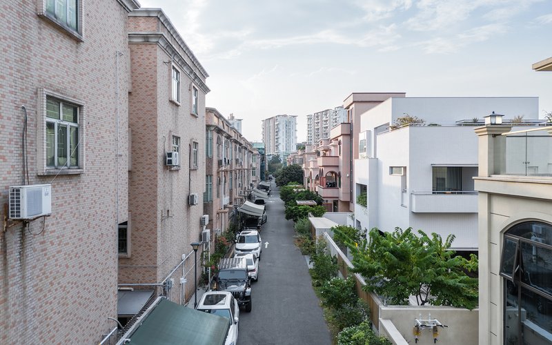 Street view between brick residential blocks with parked cars and green landscaping under cloudy skies
