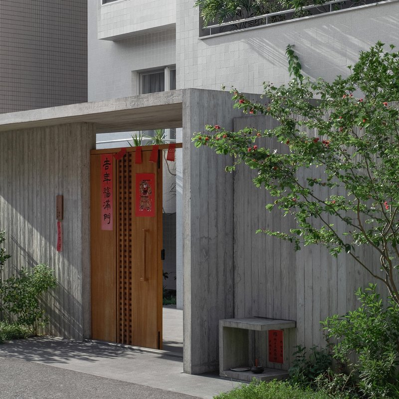 Entry courtyard with timber door and board-formed concrete walls beside a flowering tree casting shadows