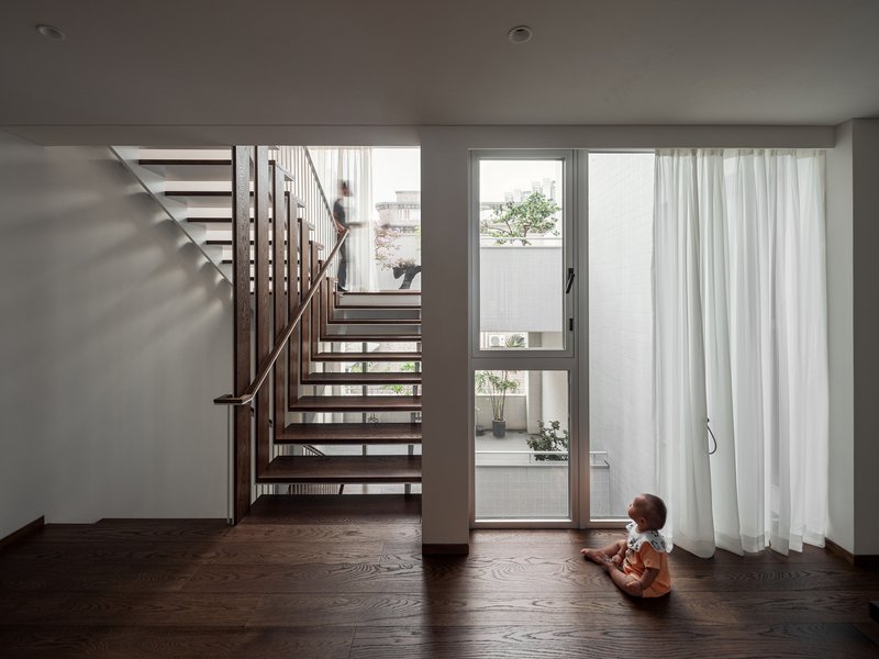 Open-tread timber staircase rising through a room where a child sits near glazed doors
