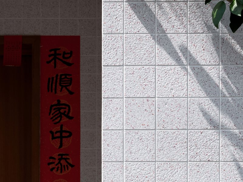 White textured tile wall with dappled shadows from a tree beside a red scroll