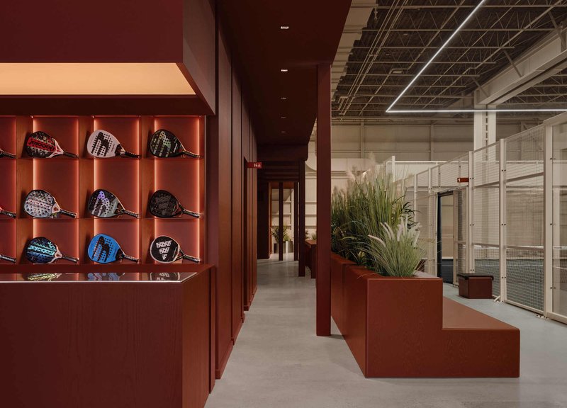 Retail interior with rust-colored millwork displaying caps beside stepped planters under an exposed truss ceiling