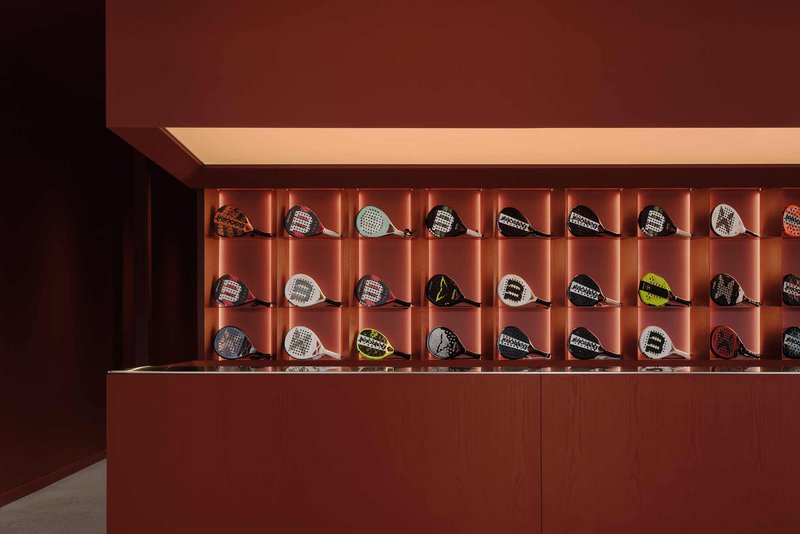 Illuminated wall display with fluted terracotta panels showcasing padel rackets on individual shelves