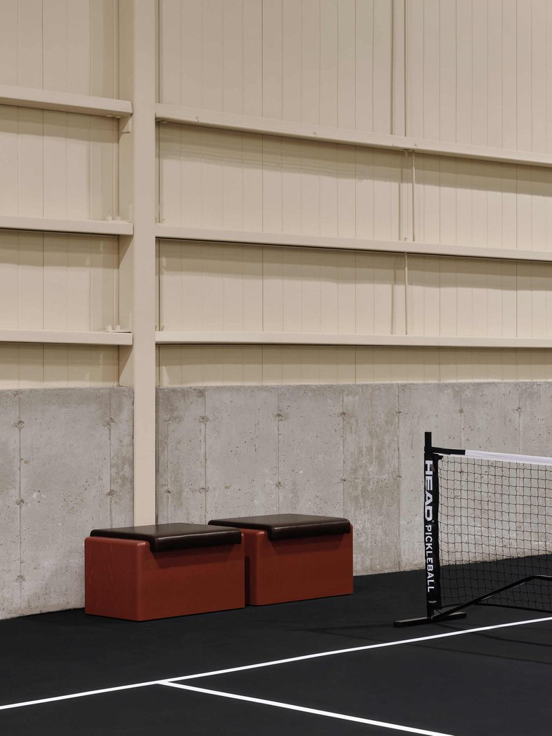 Rust-colored padded benches beside concrete wall and pickleball net on black rubber court surface