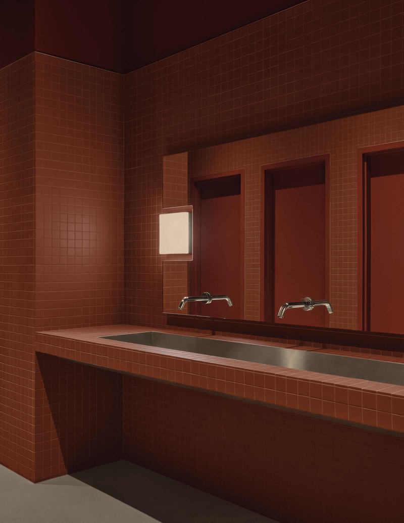 Tiled washroom corner with integrated trough sink, wall-mounted faucets and recessed mirror panel