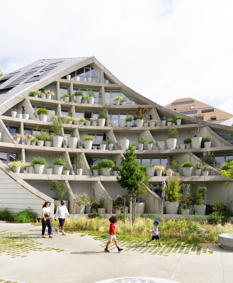 Gabled facade with exposed concrete diagonals and planted terraces as families walk through courtyard