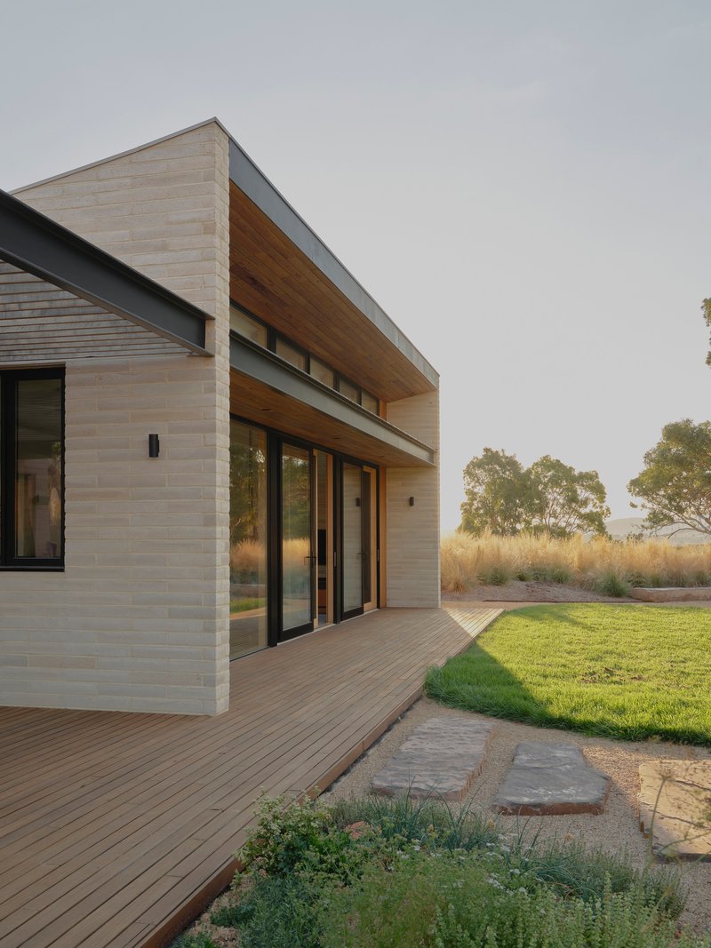 Timber deck and cantilevered overhang adjoining a mown lawn with stepping stones through gravel
