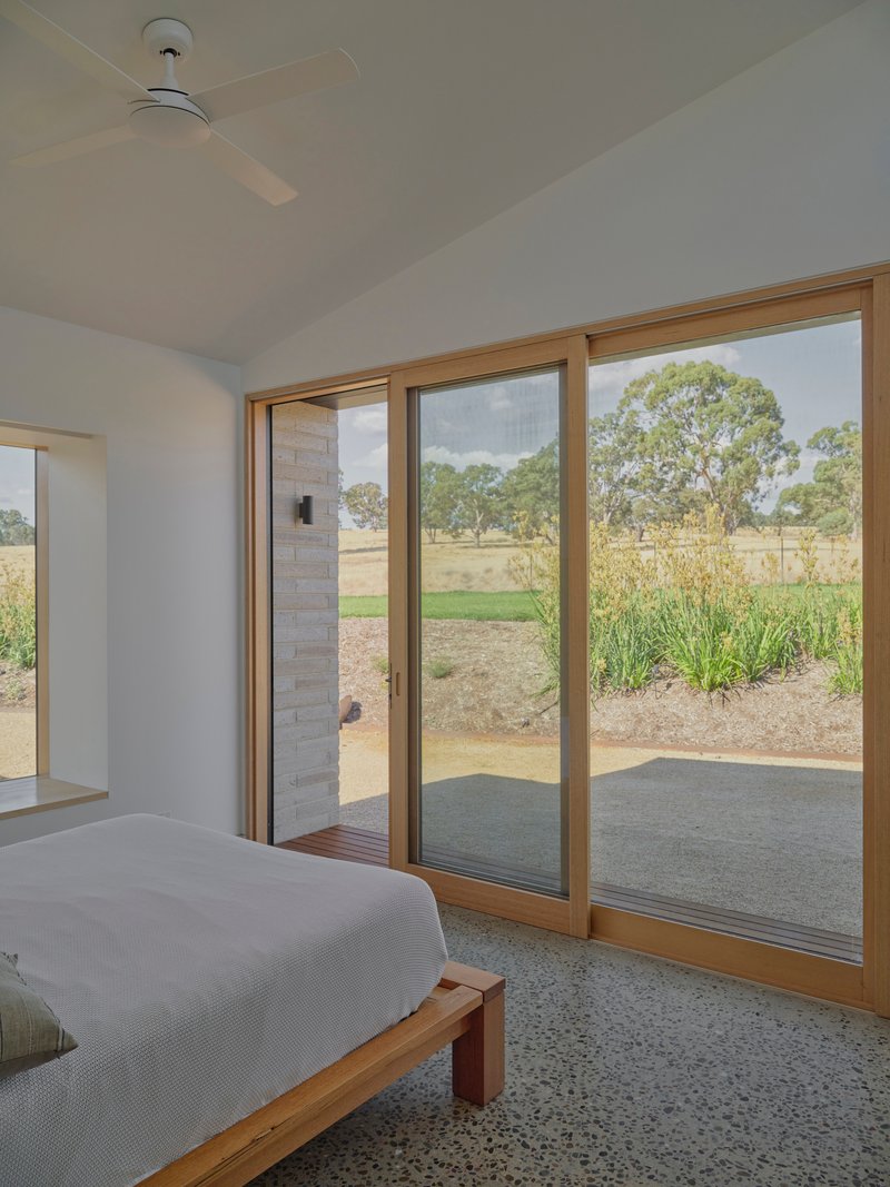 Bedroom with timber-framed sliding doors opening to a terrazzo floor and grassland beyond