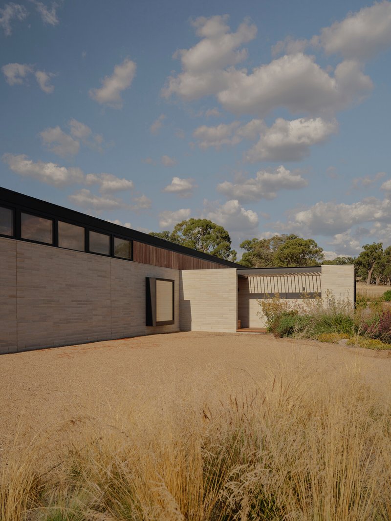 Horizontal timber and stucco facade across the courtyard with dry golden grasses in the foreground