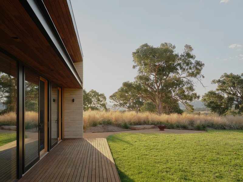 Timber deck extending from sliding glass doors toward a lawn and distant eucalyptus trees at dusk