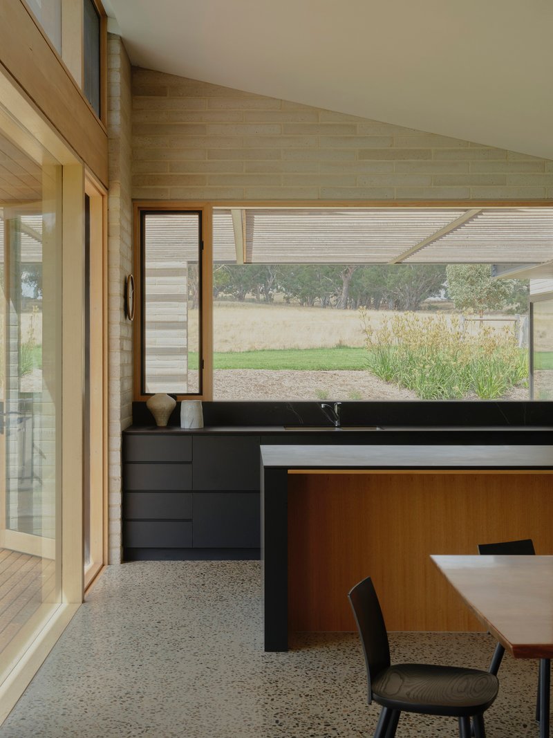 Kitchen with black countertop and timber cabinetry beneath a horizontal clerestory window overlooking the landscape