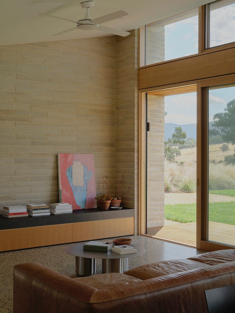 Living room with cream brick wall and full-height glazing opening to the timber deck and hillside