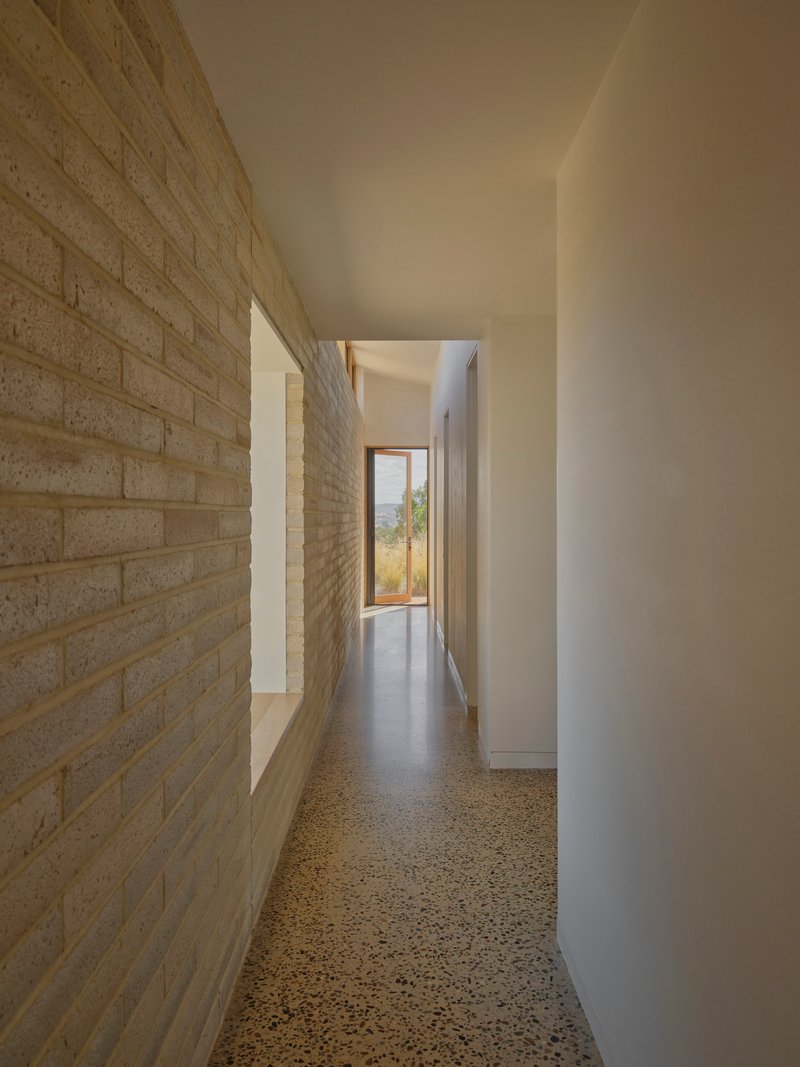 Corridor with polished concrete floor running between cream brick wall and white plaster wall toward framed view