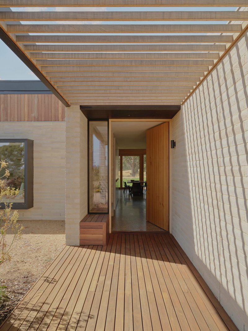 Covered entry porch with timber slatted ceiling, stone walls, and timber decking leading to glazed pivot door