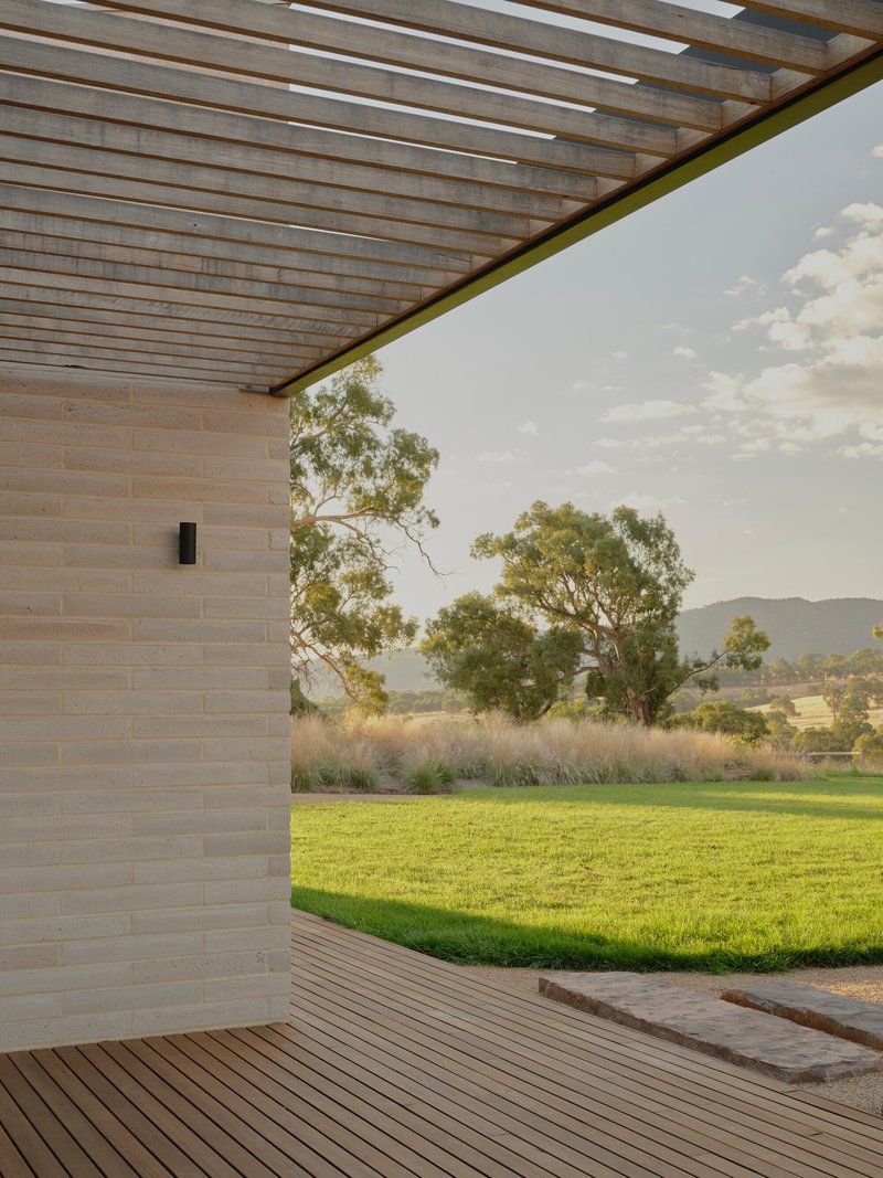 Corner of covered timber deck with slatted pergola overhead opening to lawn and distant trees
