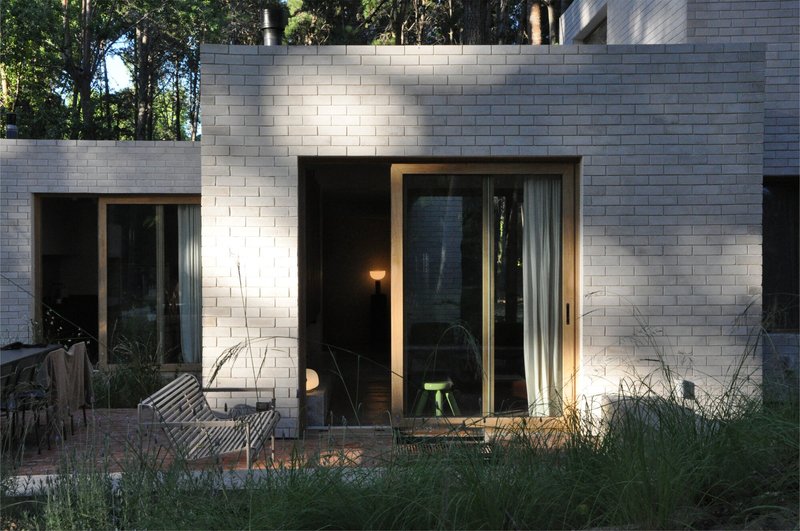 White brick facade with floor-to-ceiling glazed doors opening to a grassy courtyard at dusk
