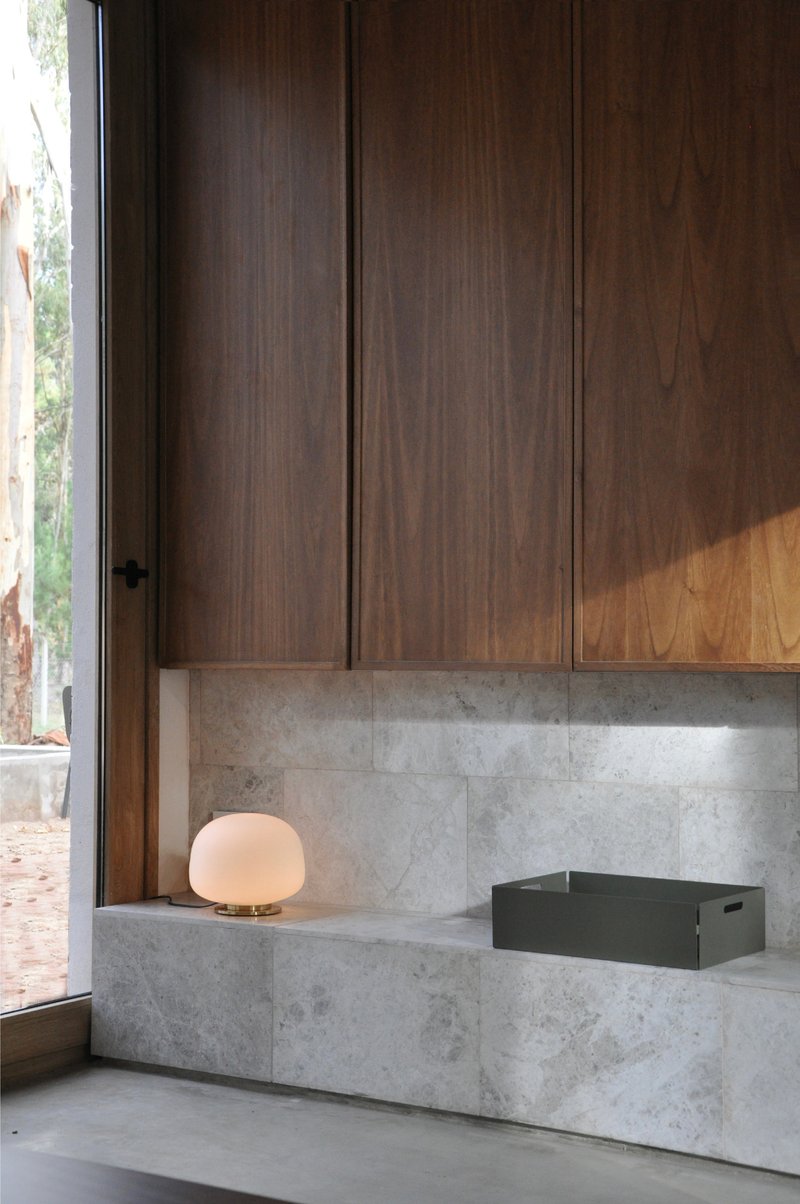 Grey stone counter with timber cabinetry and spherical lamp beside glazed door