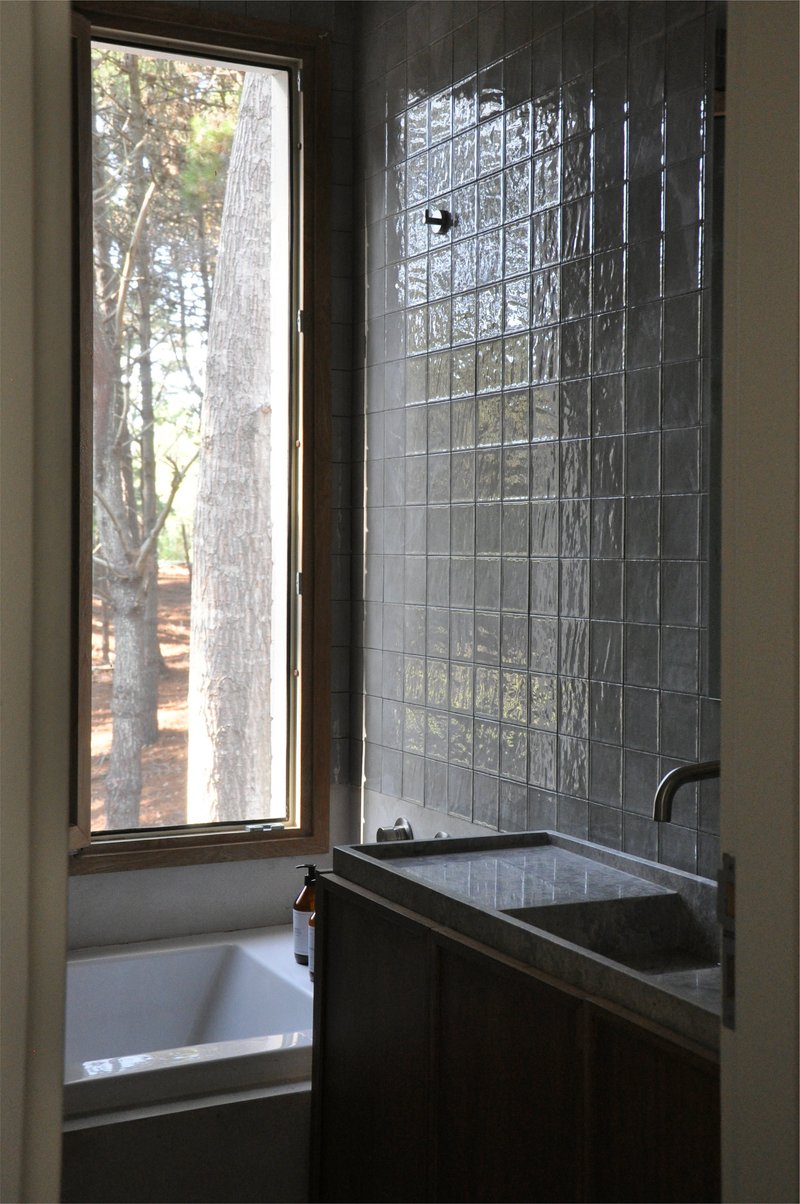 Bathroom with tall narrow window framing tree trunks, white glass tile wall and soaking tub