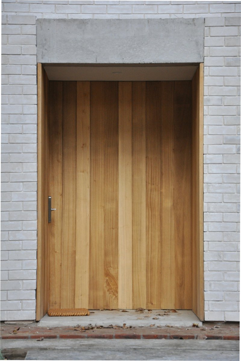 Vertical timber door set within white brick facade and concrete lintel