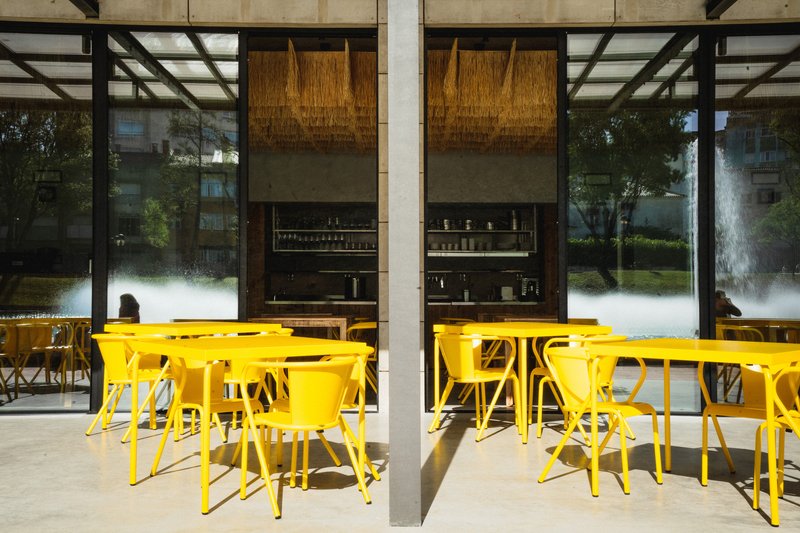Outdoor terrace seating with yellow furniture under concrete structural frame in afternoon sunlight