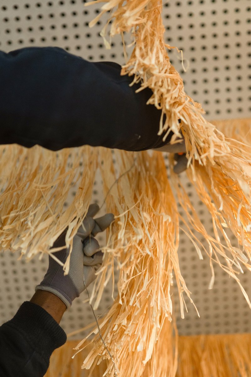 Hands holding shredded natural fiber material against a pegboard wall during assembly