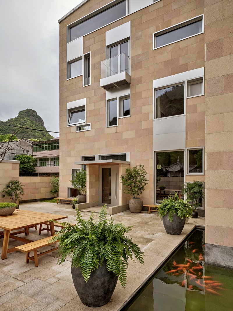 Sandstone facade with asymmetric windows overlooking courtyard koi pond with ferns in planters