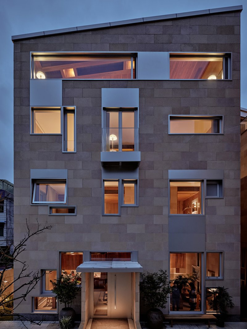 Street facade with grey block cladding and scattered windows illuminated at dusk