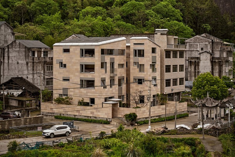 Aerial view of the rammed earth apartment block nestled among weathered village structures and lush hillside