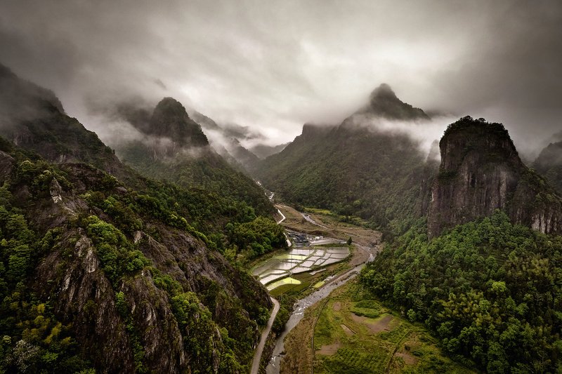 Winding river valley with terraced fields between forested karst peaks shrouded in mist