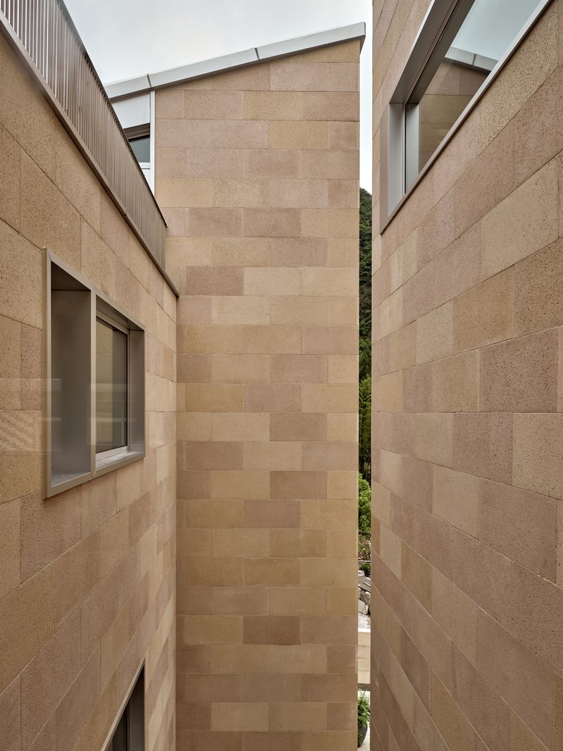 Narrow courtyard between sandstone block walls with glimpse of green hillside under an overcast sky