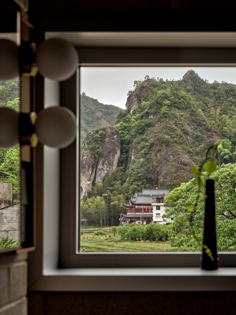 Window framing a view of forested karst mountains and a neighboring building in the valley