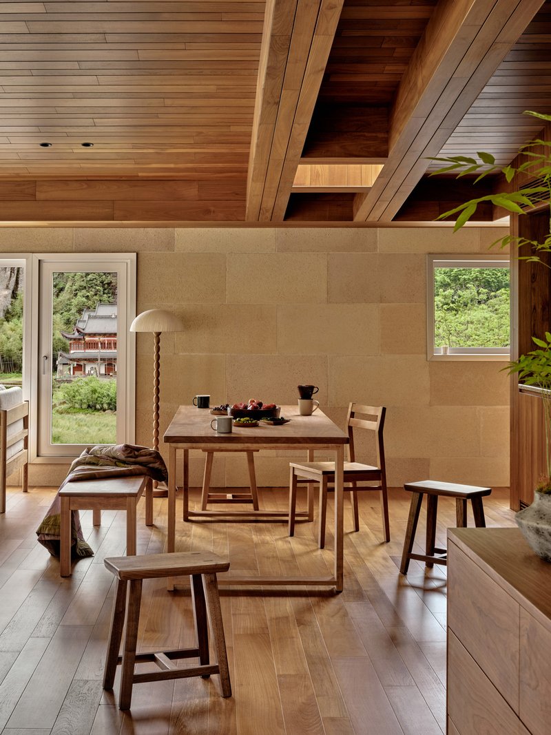 Dining area with stone block wall and angled timber ceiling beams overlooking garden through glazed doors