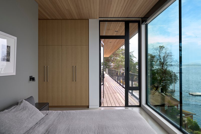 Bedroom with wood storage wall, glazed door opening to a timber deck with lake view