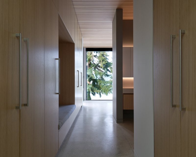 Narrow hallway lined with wood-paneled walls and concrete flooring leading to a framed view of evergreen trees