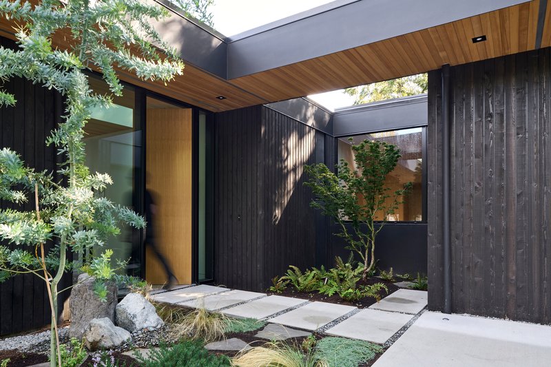 Interior courtyard with timber ceiling, charred wood walls, and stepping stones amid planted beds and boulders