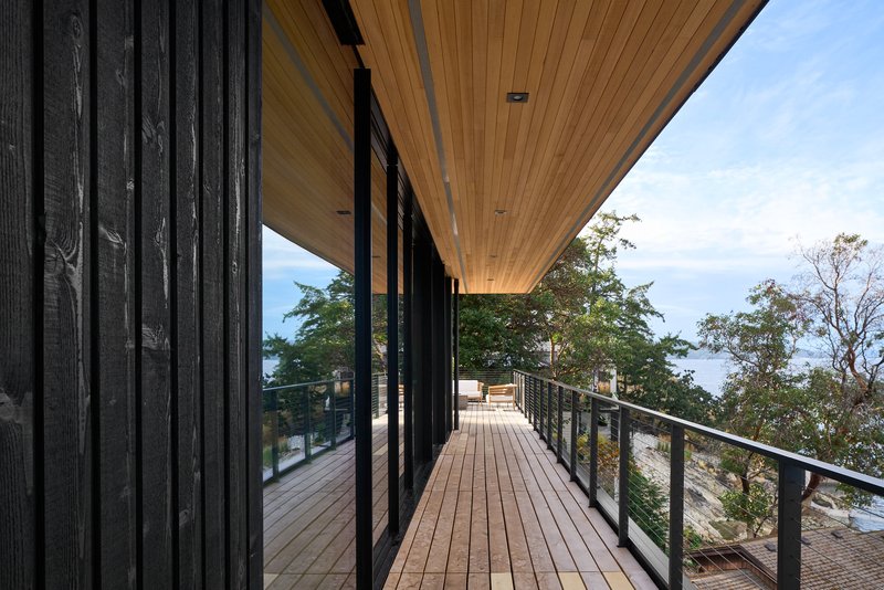 Timber deck walkway with steel railings alongside charred wood cladding under a clear blue sky