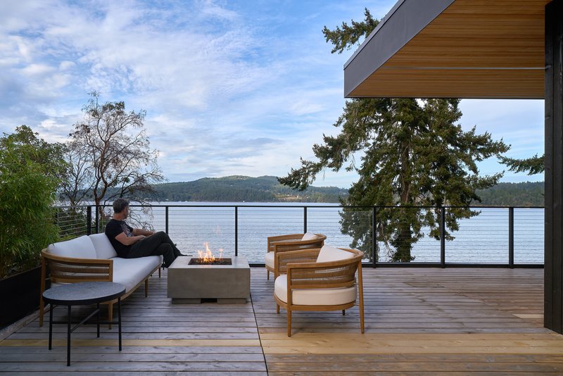 Deck terrace with a seated figure overlooking the lake through evergreens at dusk