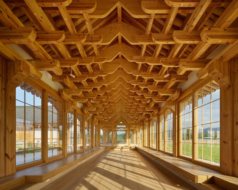 Long corridor with timber coffered ceiling and floor-to-ceiling glazing casting striped shadows on the floor