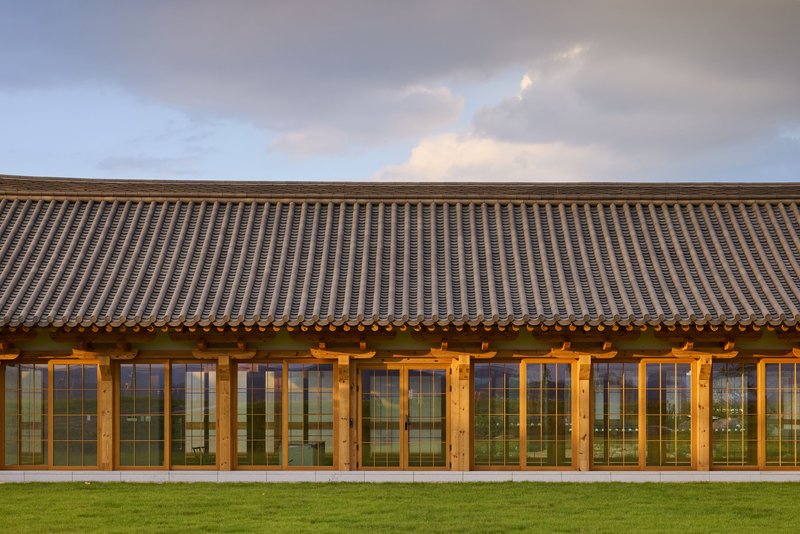 Exterior facade with repeating timber-framed glazed doors beneath a sweeping tile roof at dusk