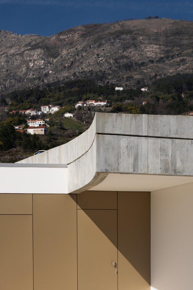 Curved concrete parapet meeting tan paneled wall with a hillside dotted with houses in the background