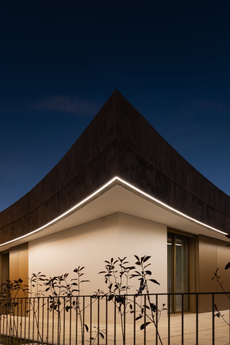 Illuminated roof edge above the white facade corner with bamboo plants behind a metal railing