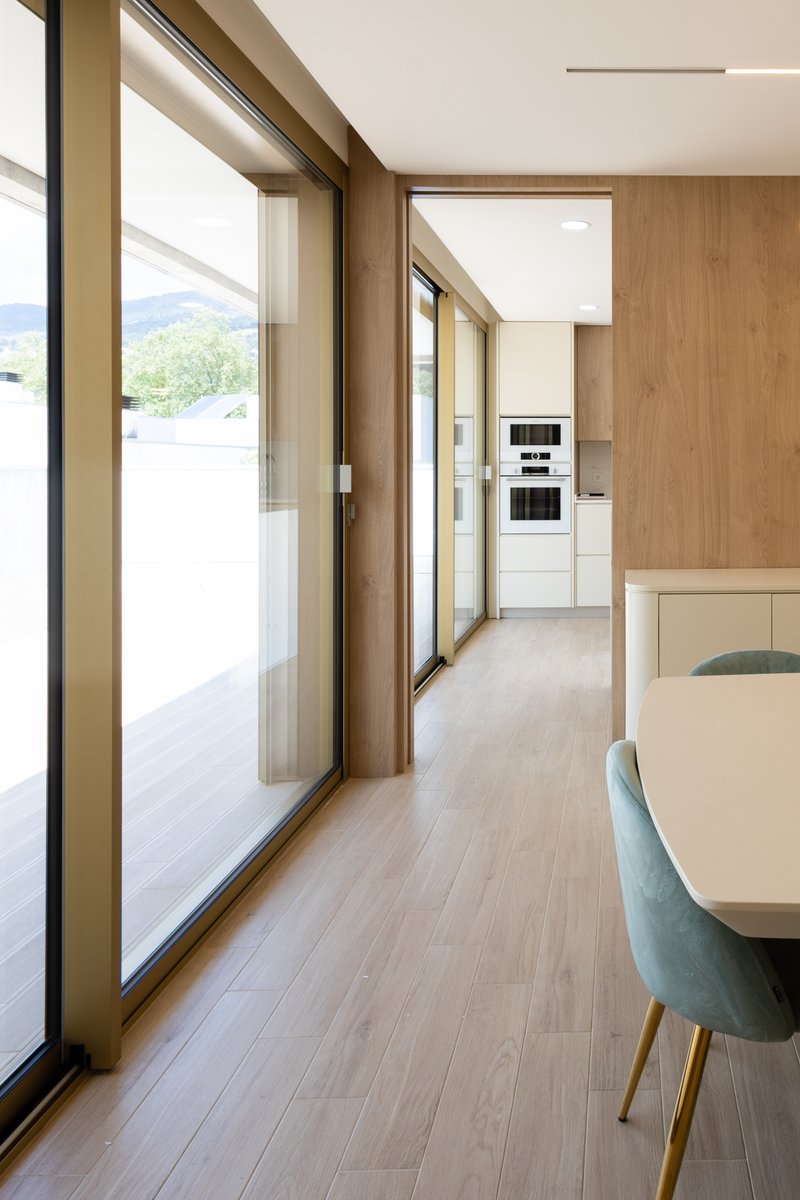 Interior corridor with floor-to-ceiling glazing, timber panels and pale wood flooring opening to distant hills
